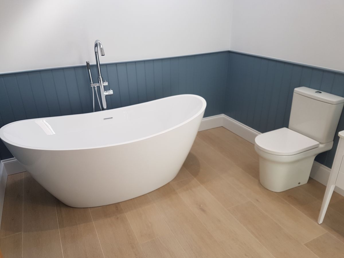A freestanding bath with a floor-standing tap against blue tongue-and-groove panelling