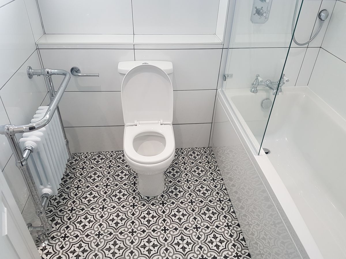 A bathroom with white wall tiles, a black and white patterned floor and a traditional chrome radiator