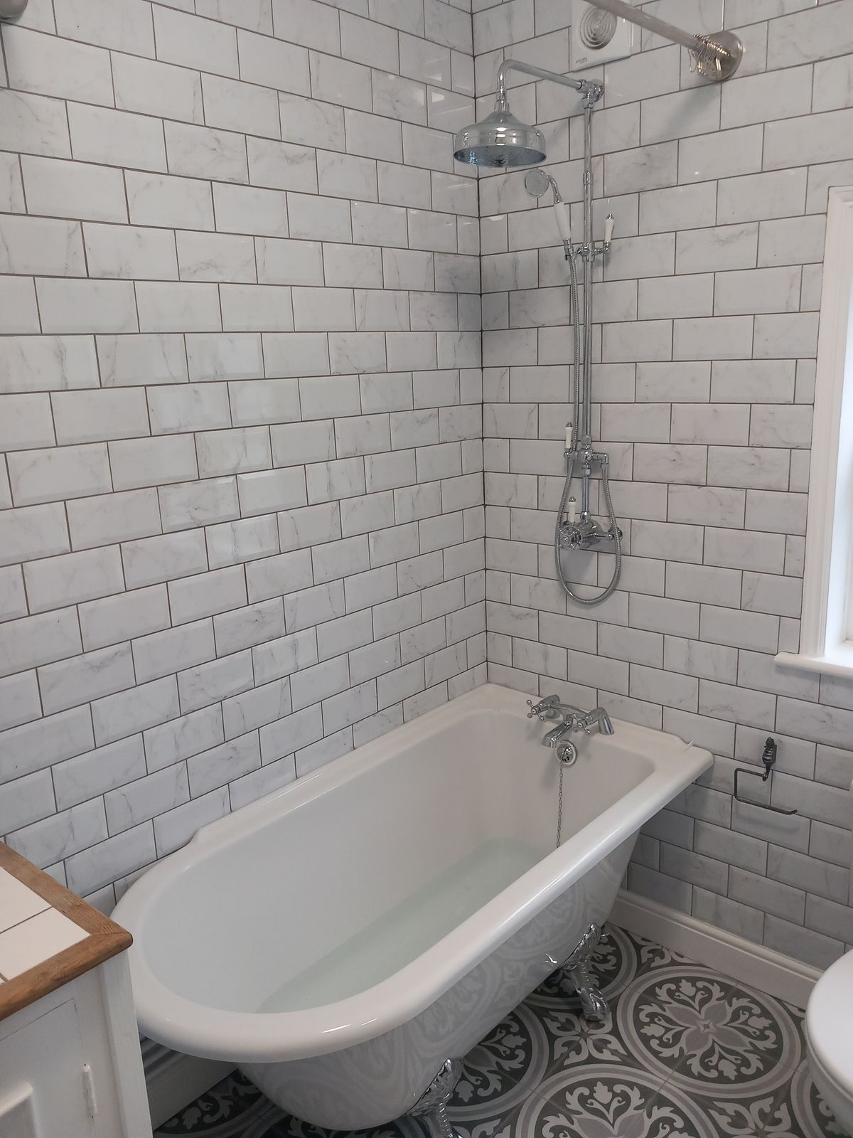 A roll-top bath with a traditional shower, white metro tiles and a patterned floor