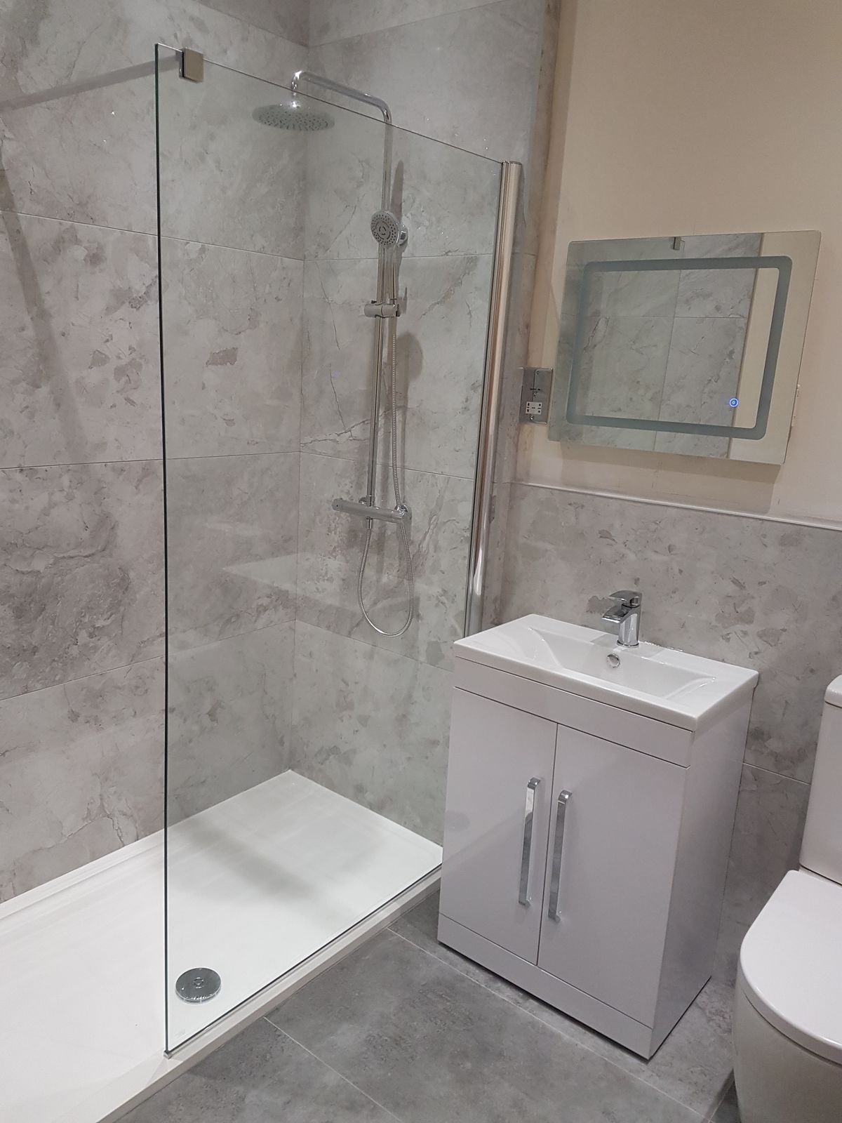 A walk-in shower with grey marble-effect tiles, a rainfall shower head and an LED mirror
