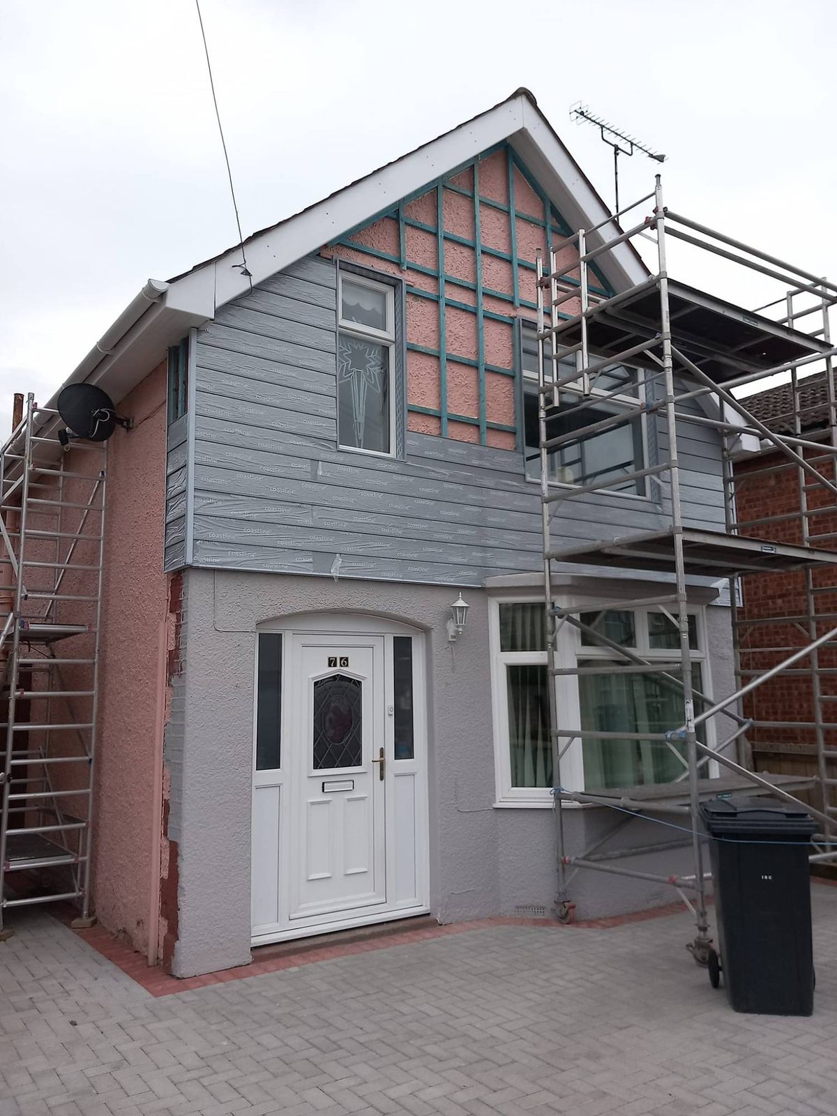 A house part-way through new grey cladding on the upper storey, with scaffold towers either side